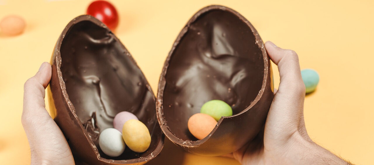 mãos de homem segurando um ovo de Páscoa partido ao meio com pequenos ovinhos de chocolate dentro