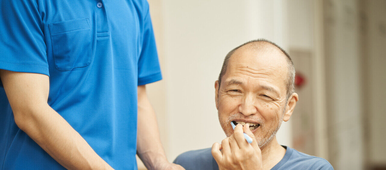 idoso escovando os dentes ao lado de um cuidador