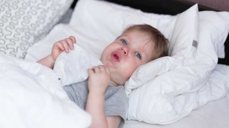bebê deitando na cama com tosse, segurando um lenço
