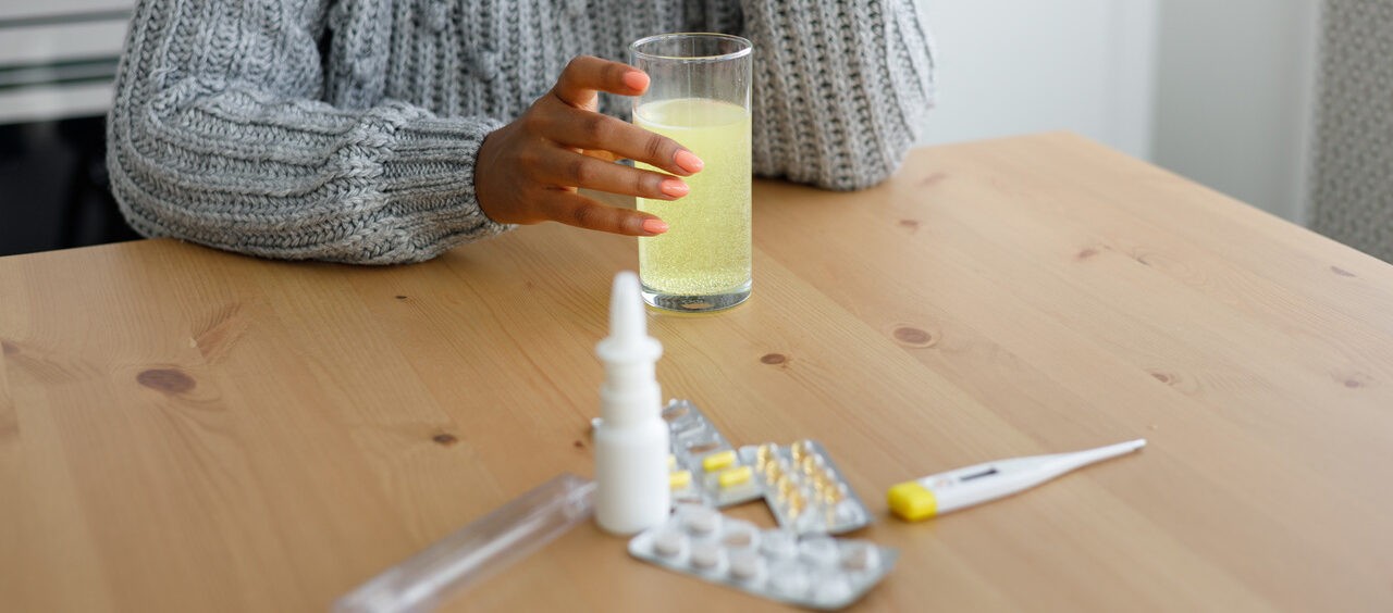 mulher sentada na mesa da cozinha com remédios para gripe na sua frente