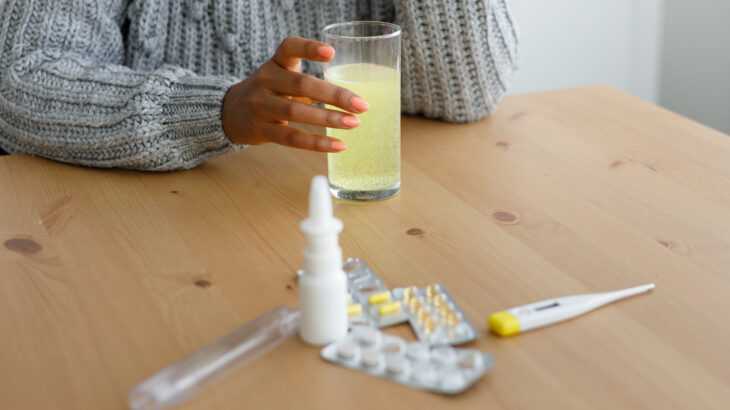 mulher sentada na mesa da cozinha com remédios para gripe na sua frente