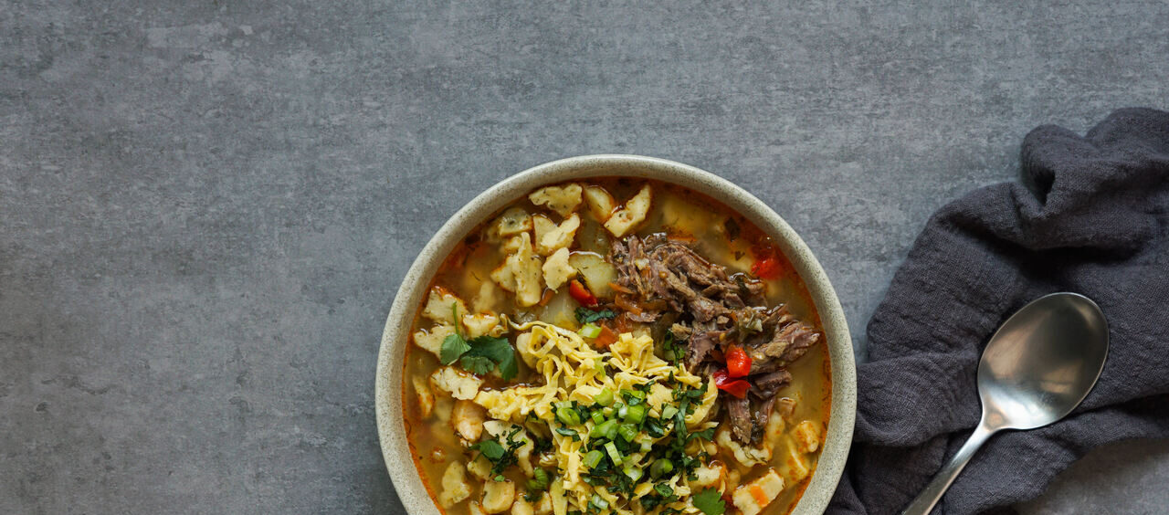 cumbuca com sopa vista de cima ao lado de um guardanapo de pano e uma colher
