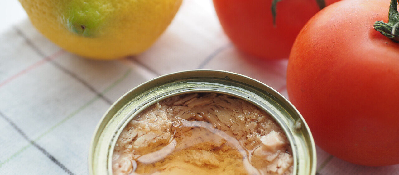 lata de atum aberta em cima de um pano de prato e ao lado de tomates e de um limão siciliano