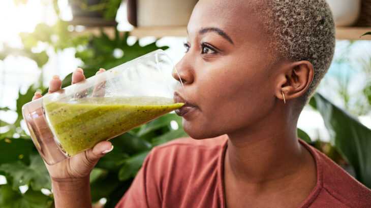 mulher de lado tomando um suco verde em um copo