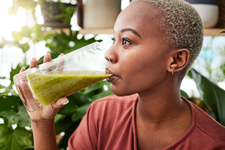 mulher de lado tomando um suco verde em um copo