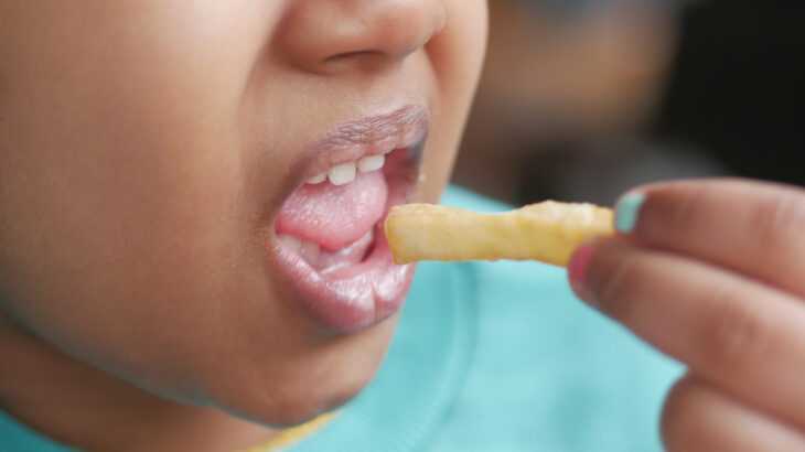 criança com sobrepeso comendo uma batata frita