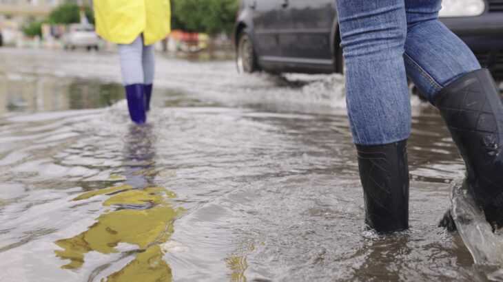 pés de pessoas calçando botas andando no meio de uma enchente