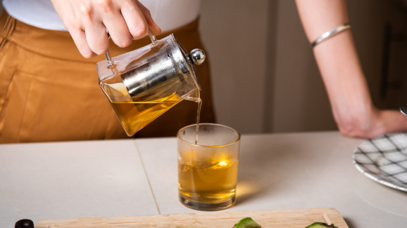 mulher colocando chá em uma xícara, em cima de uma mesa de madeira. o consumo de chá traz muitos beneficios a saúde.