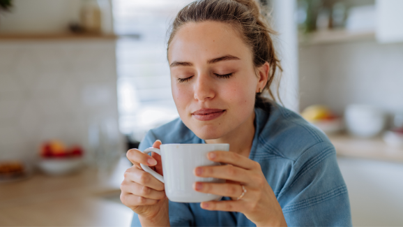 mulher de olhos fechados segurando uma caneca branca com chá para cólica menstrual