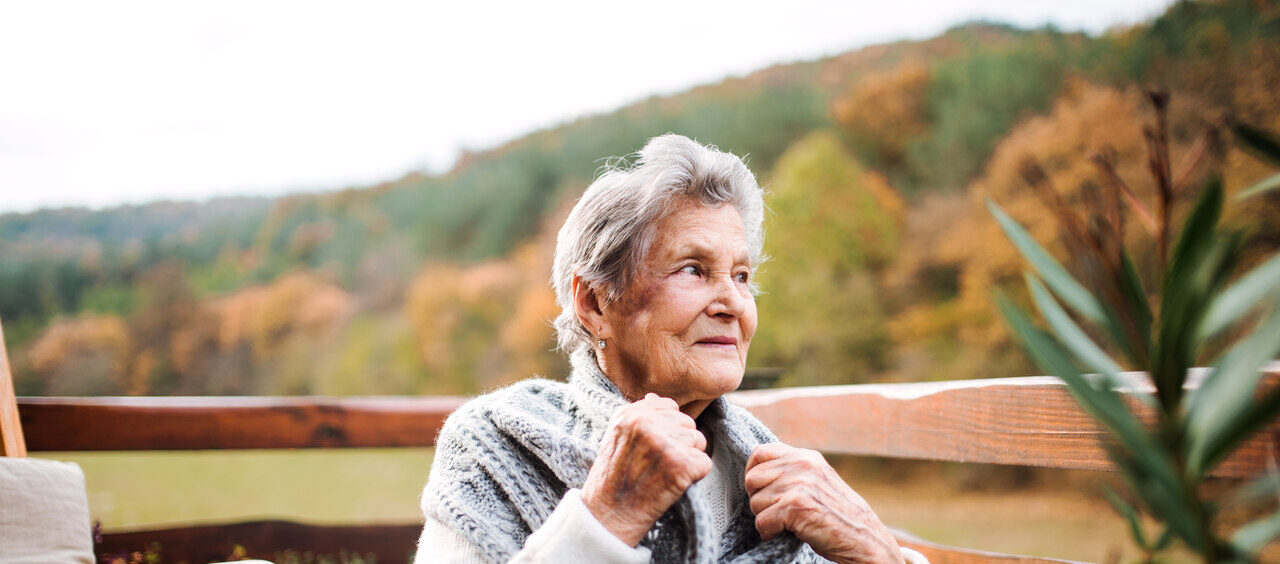 senhora sentada na sacada de casa com um casaco