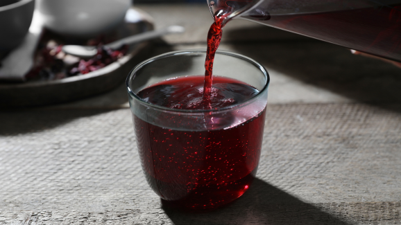 Chá de hibisco, que pode causar interação medicamentosa se misturado com alguns remédios, em um copo de vidro em cima de uma mesa cinza.