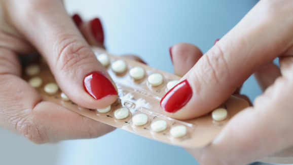 Imagem aproximada das mãos de uma mulher segurando um método contraceptivo oral