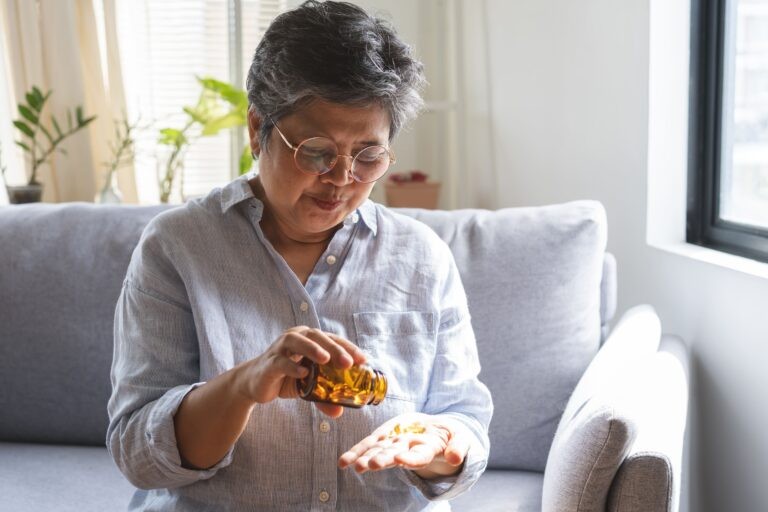 mulher sentada no sofá com um frasco de vitaminas essenciais para idosos.