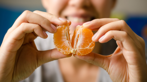 mulher segurando uma laranja ao meio, uma fruta da dieta-anti-inflamatória